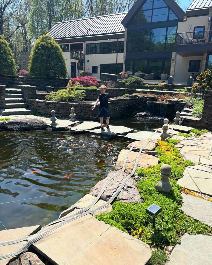 A young boy standing on stepping-stones across a custom backyard koi pond built by JK-Fish