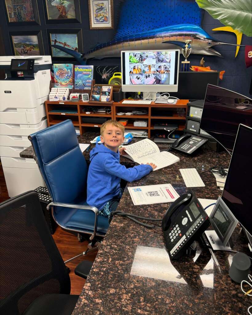 A young boy at the JK-Fish office on Bring Your Kid to Work Day, with a mounted sailfish on the wall behind him